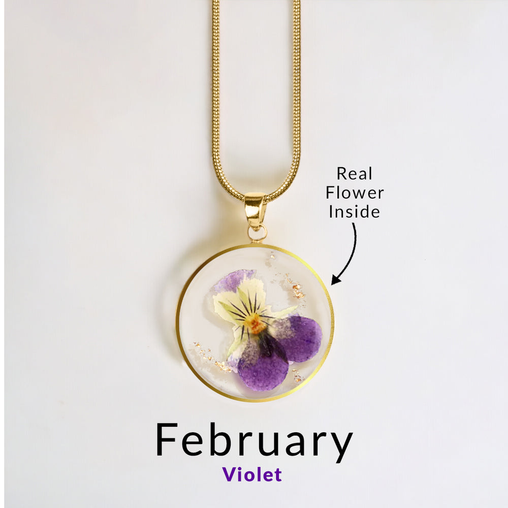 A gold-colored snake chain necklace with a round resin pendant containing a real red flower.