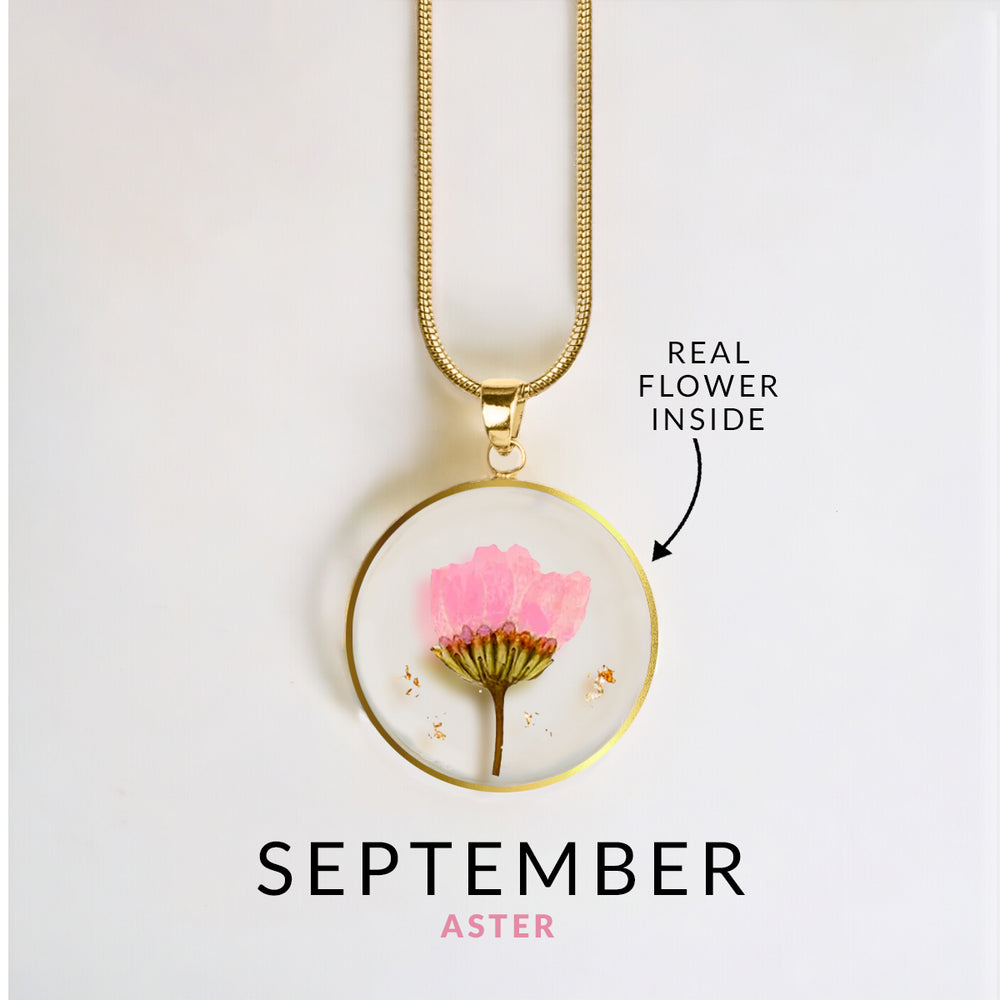 A gold-colored snake chain necklace with a round resin pendant containing a real red flower.