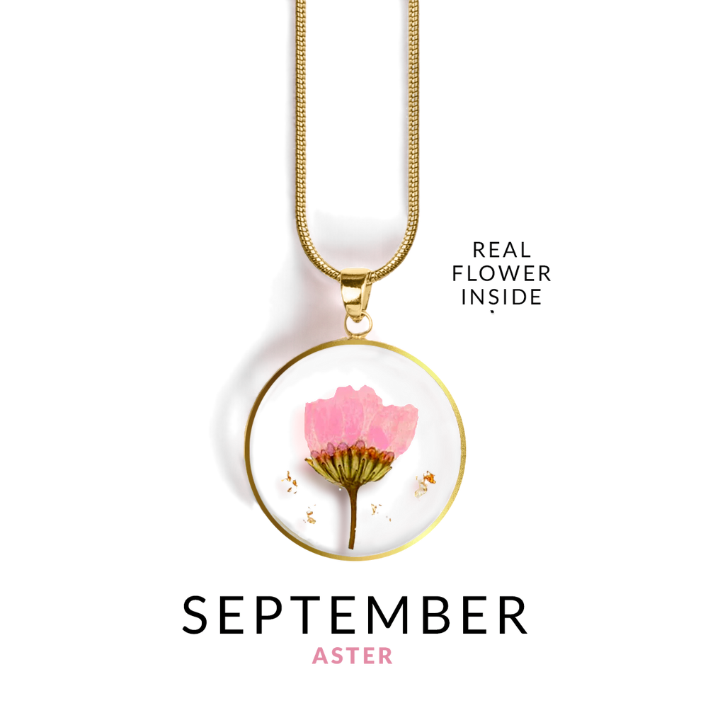 A gold-colored snake chain necklace with a round resin pendant containing a real red flower.