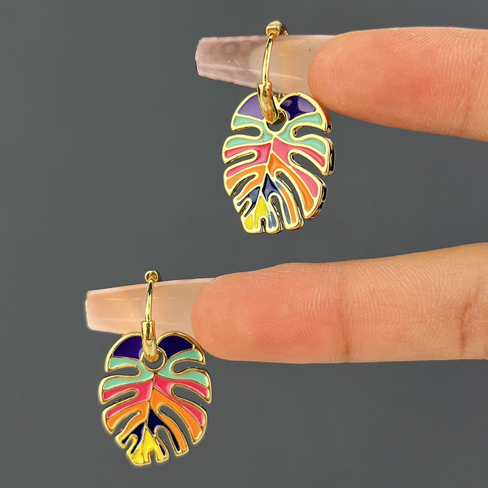 A pair of gold-plated earrings shaped like a monstera leaf with a rainbow pattern.