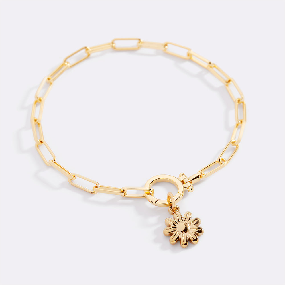Gold bracelet with a sunflower charm on a light gray background