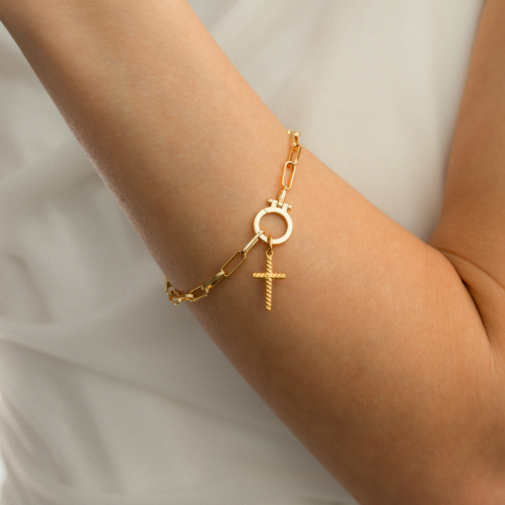 Gold bracelet with a cross charm on a person's wrist against a neutral background