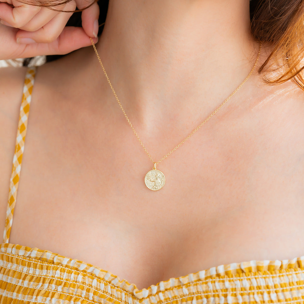 Gold necklace with a pendant worn by a person in a yellow top.