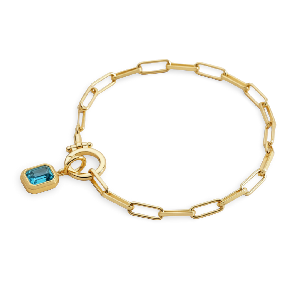 Gold bracelet with a blue gemstone charm on a light gray background