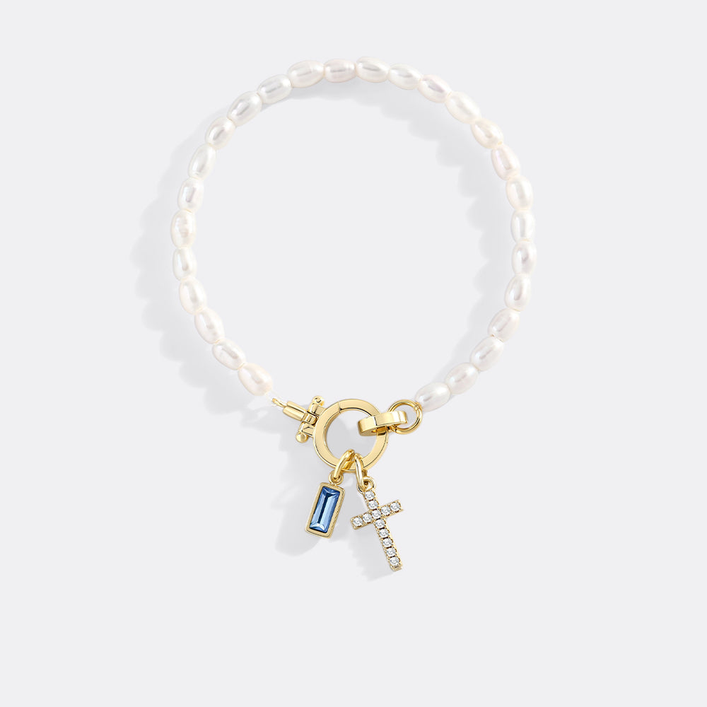Pearl bracelet with gold charm and blue gemstone on a light gray background