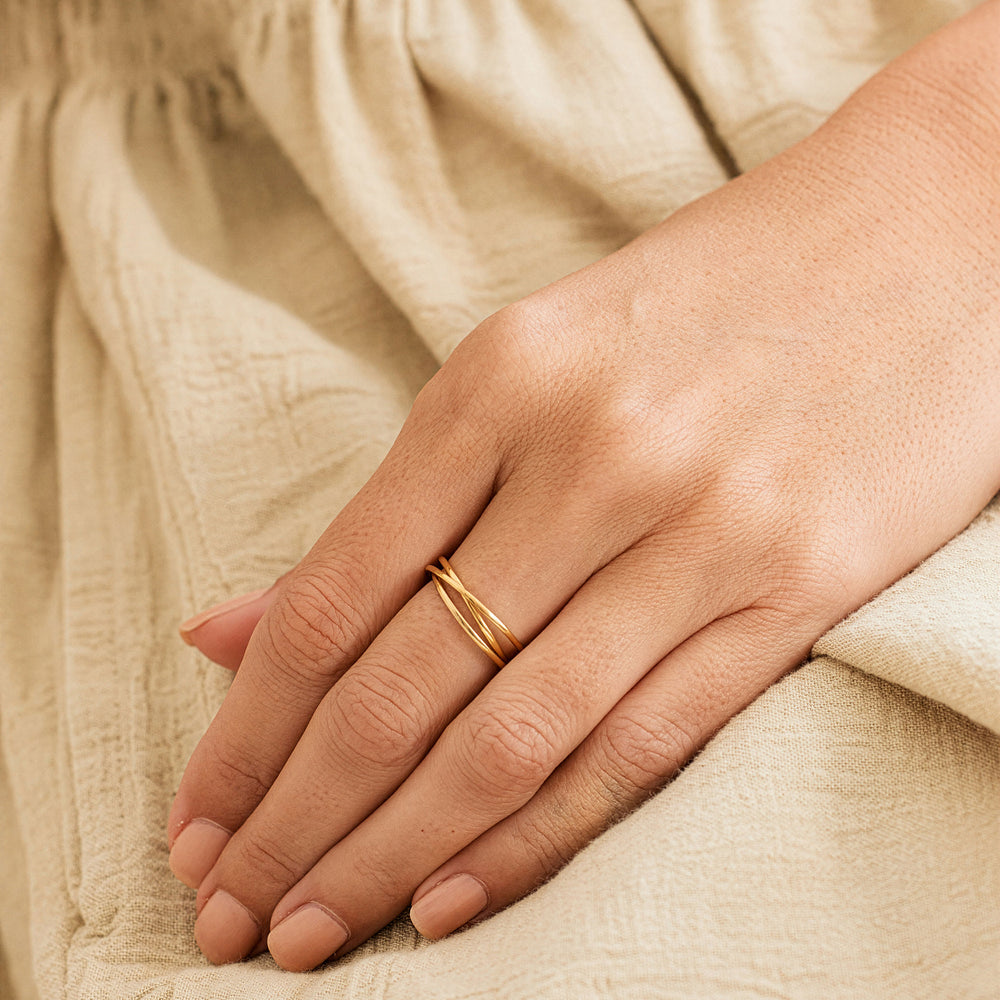 A hand wearing a gold interlocking fidget ring on a beige textured background.