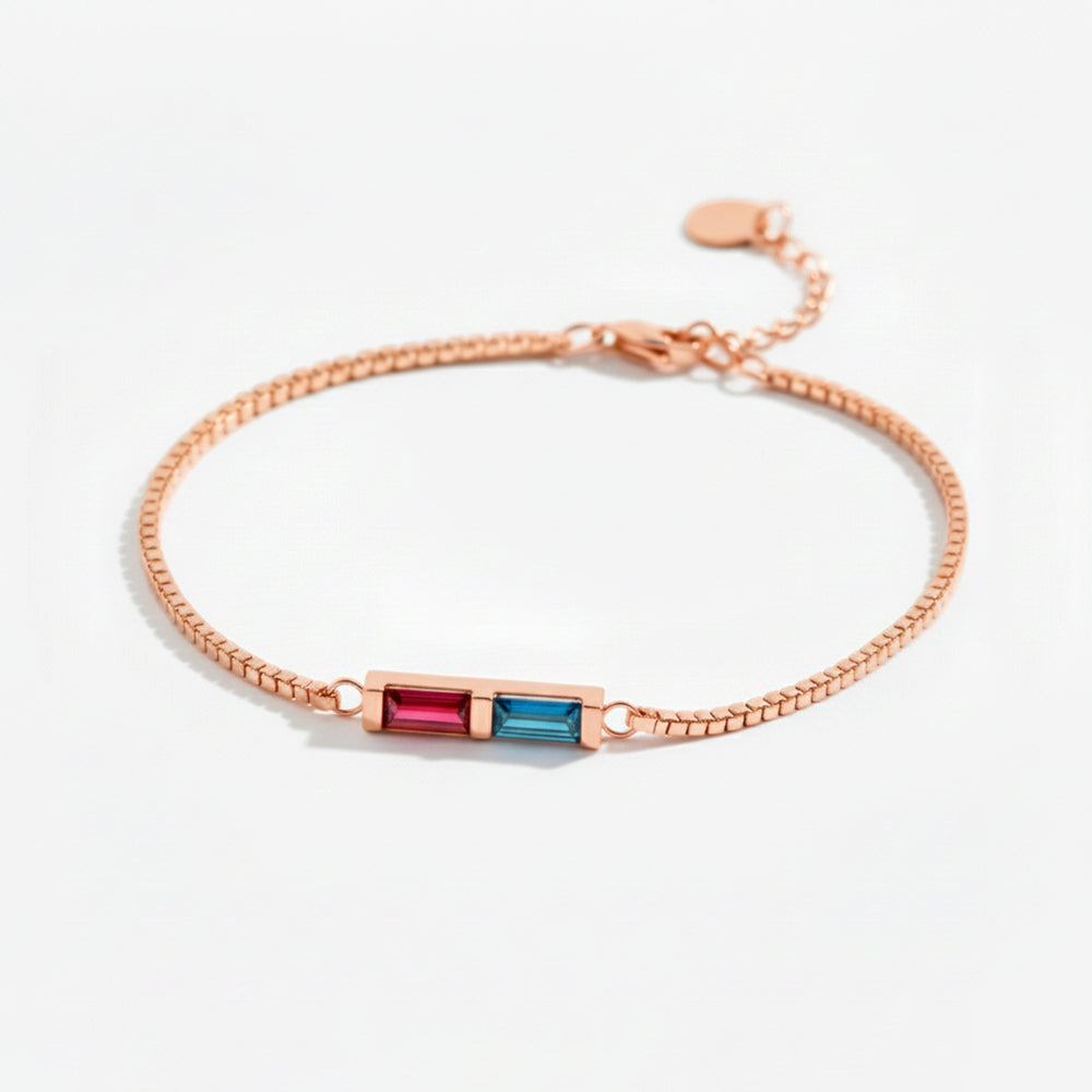 Rose gold bracelet with red and blue gemstones on a light gray background