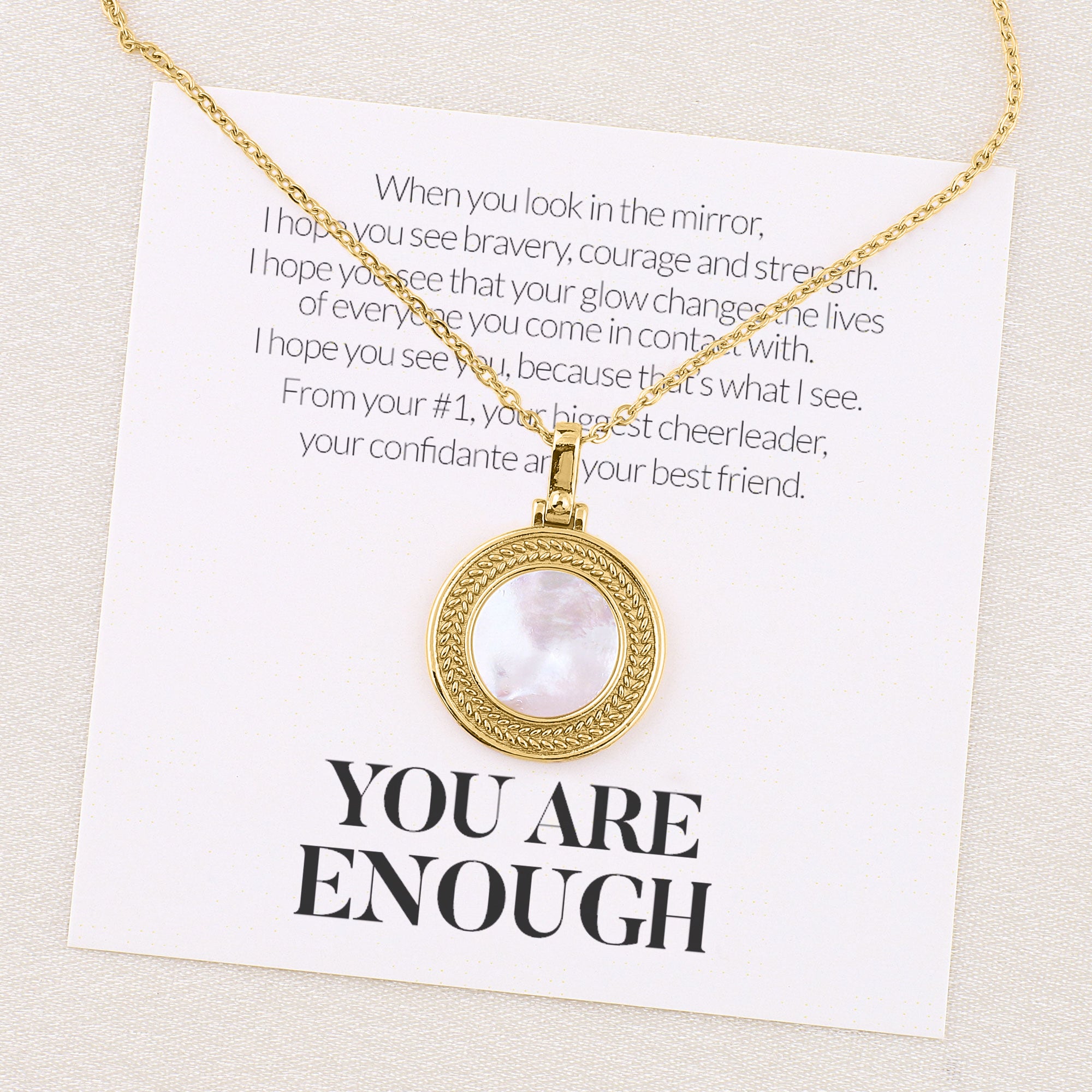 A gold-toned necklace with a pearl-like bead and a meaningful card attached, displayed against a neutral background.