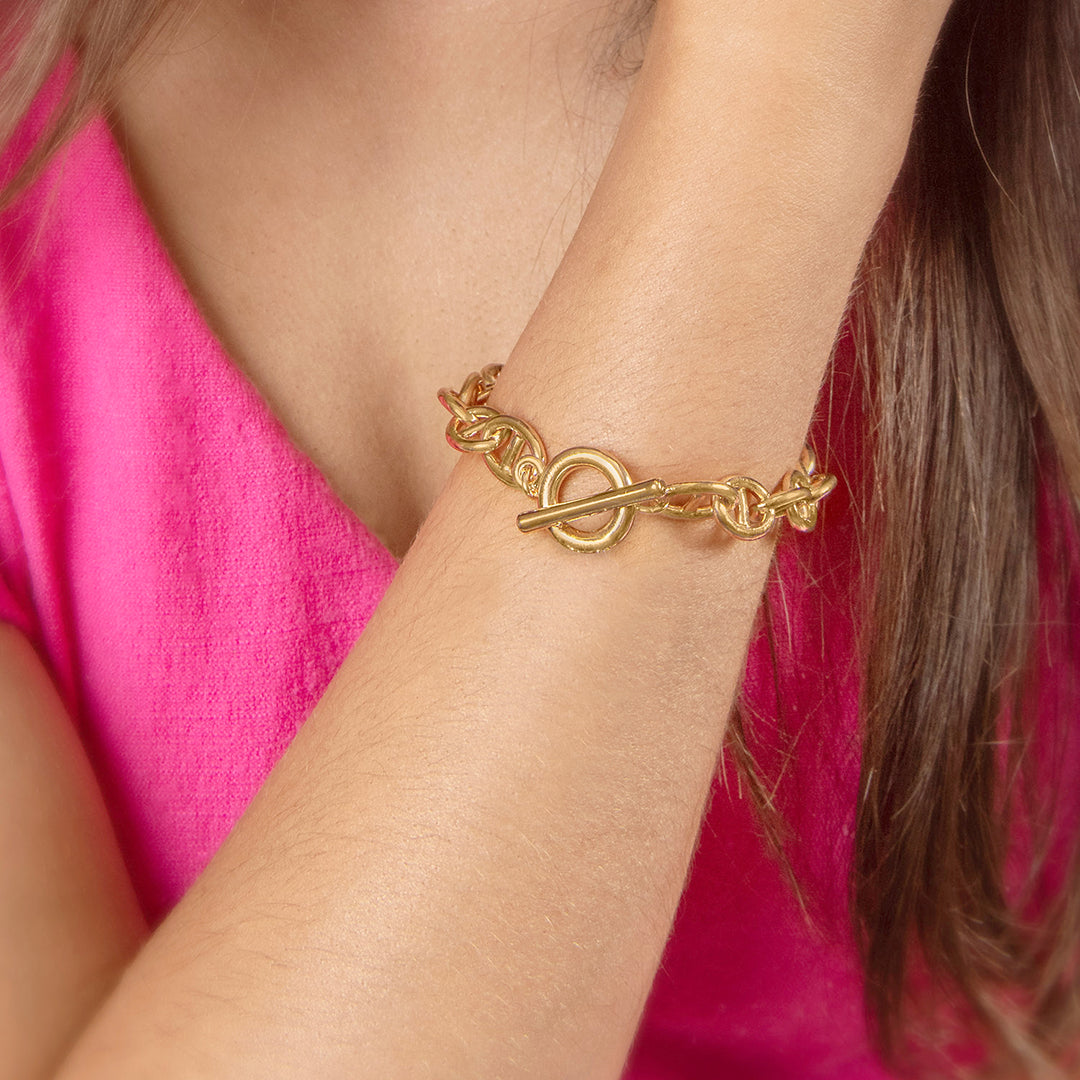 A person wearing a gold-colored bracelet with an oversized anchor chain design on their wrist.